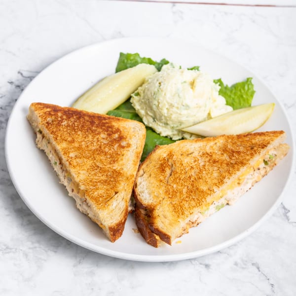Grilled cheese sandwich halves, potato salad, and pickle spears on a white plate.