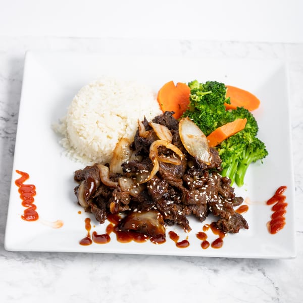 Teriyaki beef with onions, sesame seeds, white rice, broccoli, and carrots on a white plate.