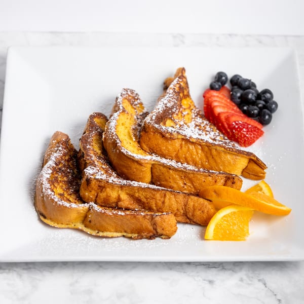 Golden French toast slices dusted with powdered sugar, served with fresh strawberries, blueberries, and orange wedges.