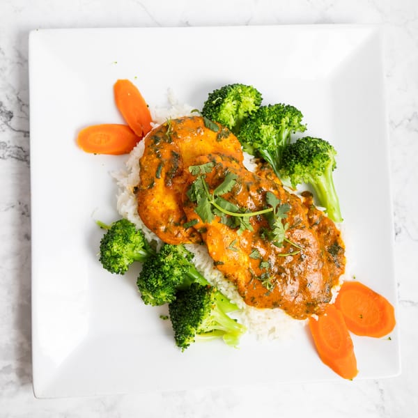 Two pieces of chicken in orange sauce with cilantro, served over rice with broccoli and carrots.
