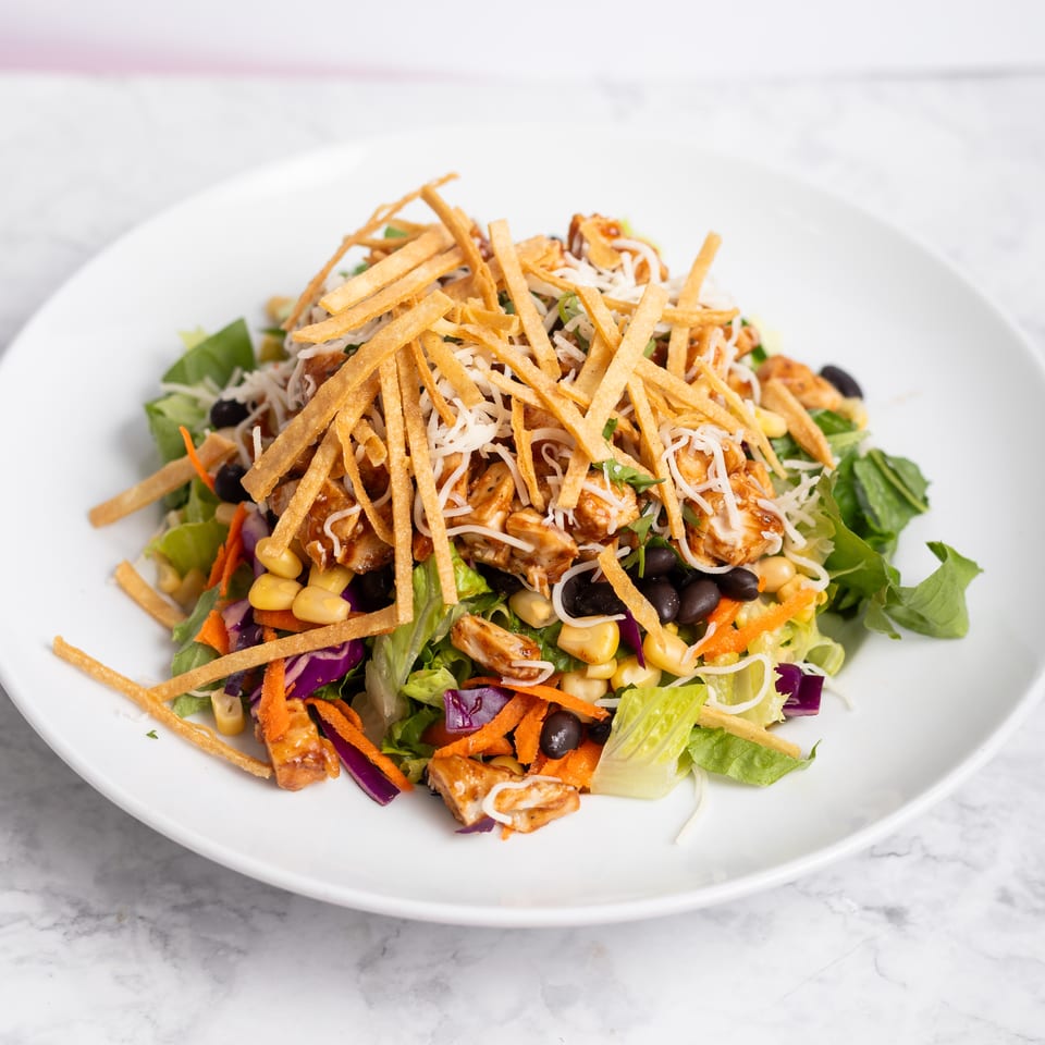 A vibrant salad with grilled chicken, corn, black beans, shredded cheese, and crispy tortilla strips.