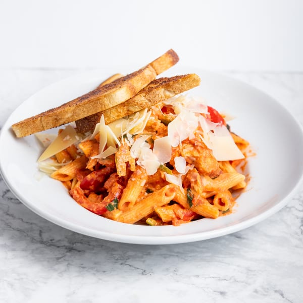 Penne pasta in a creamy red sauce with chicken, vegetables, parmesan, and toasted bread.