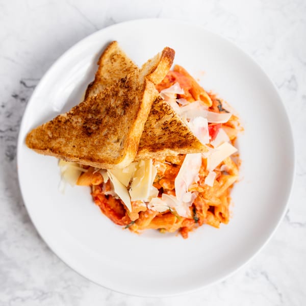 Penne pasta in red sauce with shaved parmesan and two pieces of toasted bread on a white plate.