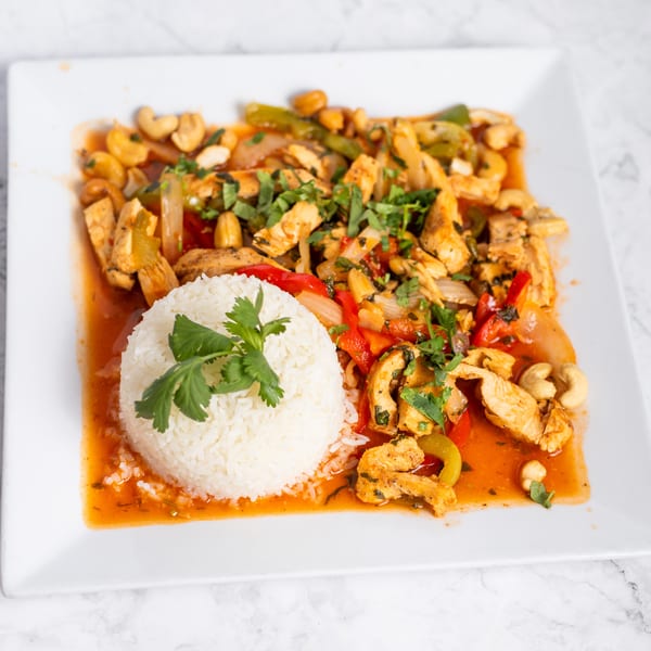 Chicken stir-fry with cashews, peppers, onions, and rice on a white plate.