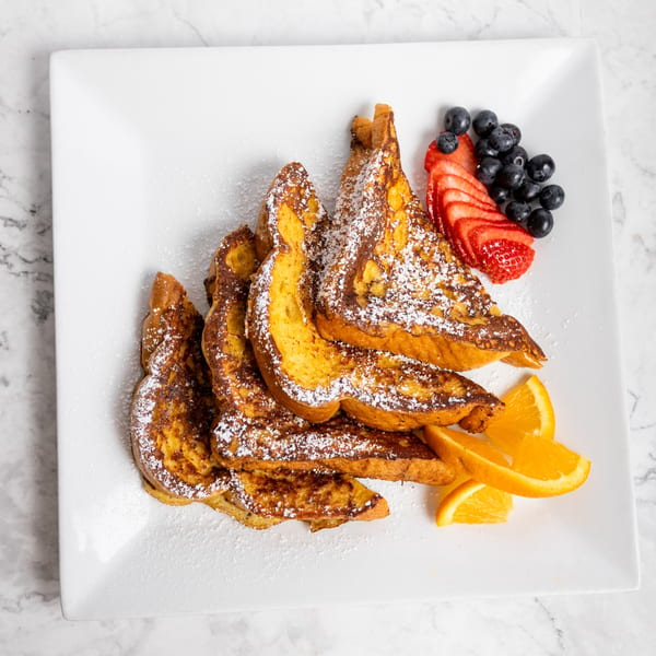 Golden French toast dusted with powdered sugar, served with fresh blueberries, sliced strawberries, and orange wedges.