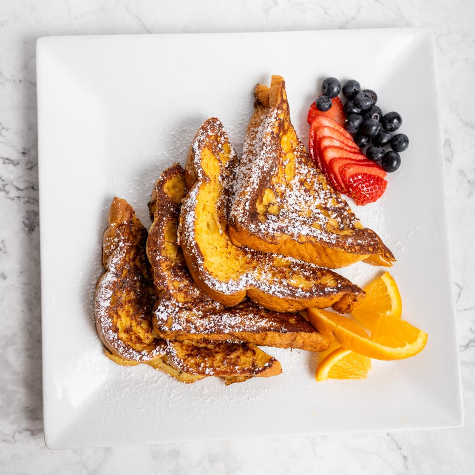 Golden French toast dusted with powdered sugar, served with fresh blueberries, sliced strawberries, and orange wedges.