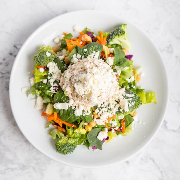 A vibrant salad with mixed greens, broccoli, carrots, chickpeas, and feta cheese on a white plate.