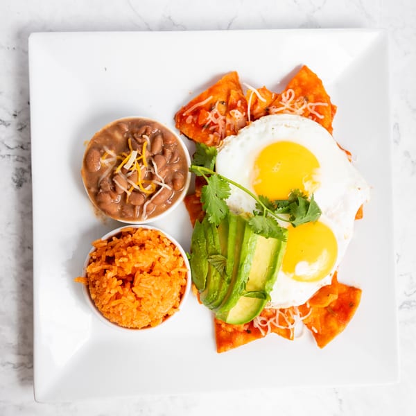 Chilaquiles with two fried eggs, avocado, cilantro, refried beans, and Mexican rice.