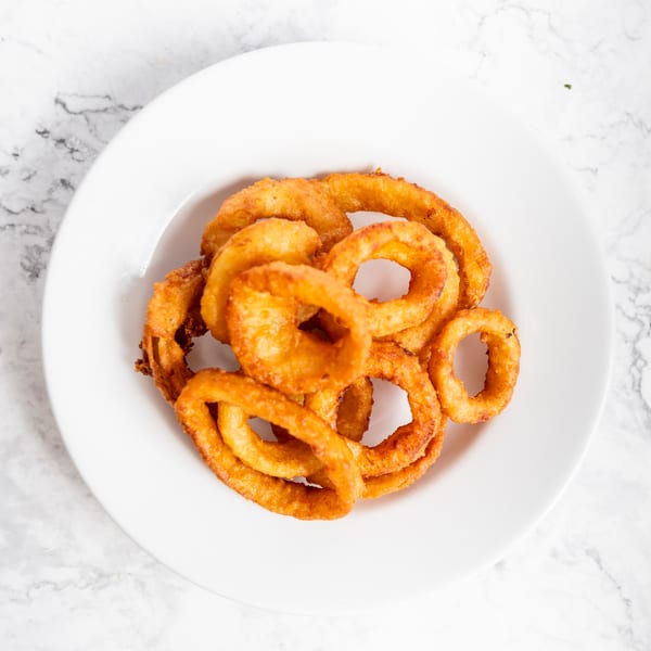 A white plate filled with golden-brown, crispy onion rings on a marble surface.