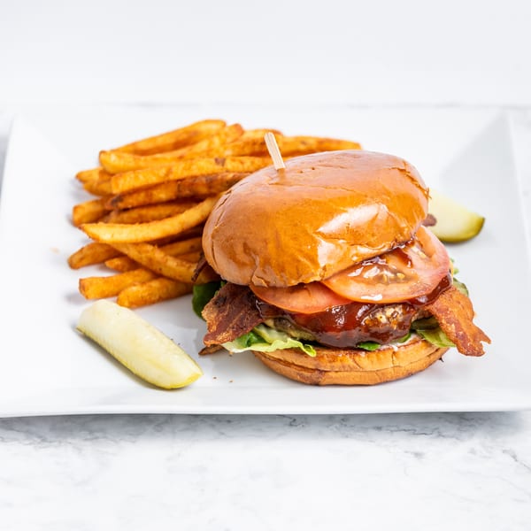 A bacon cheeseburger with lettuce, tomato, and BBQ sauce, served with fries and pickles.