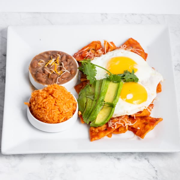 Chilaquiles with two fried eggs, sliced avocado, cilantro, refried beans, and orange rice.
